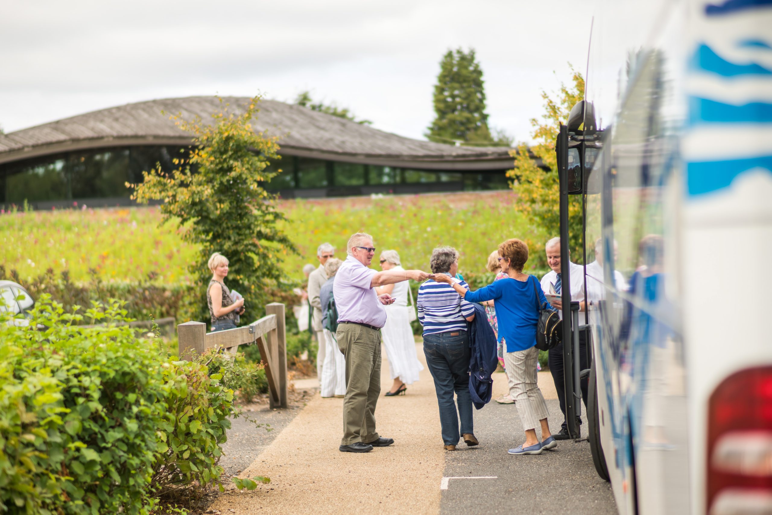 A group of people disembarking a coach at The Savill Garden Visitor Centre car park.
