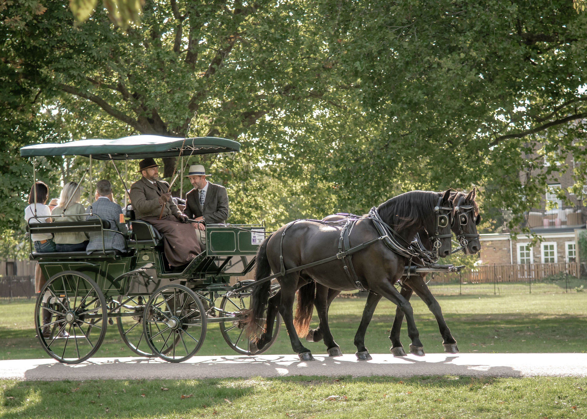 A green and gold carriage with two black horses. Adults are sitting in the carriage.