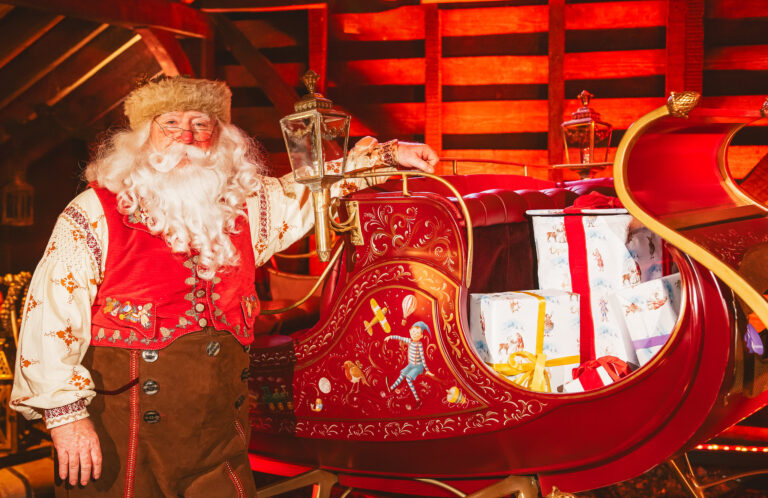 Father Christmas stood next to his sleigh filled with gift-wrapped presents.