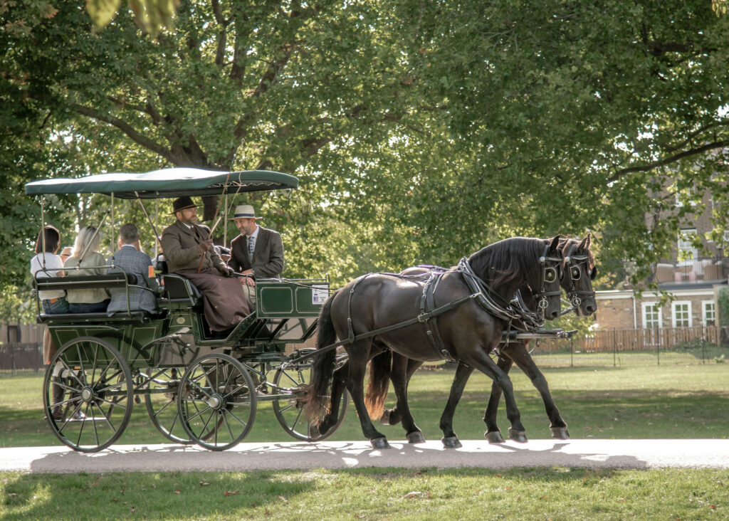 A green and gold carriage with two black horses. Adults are sittin in the carriage
