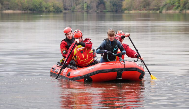 Four people on a red dingy in Virginia Water Lake wearing safety clothing