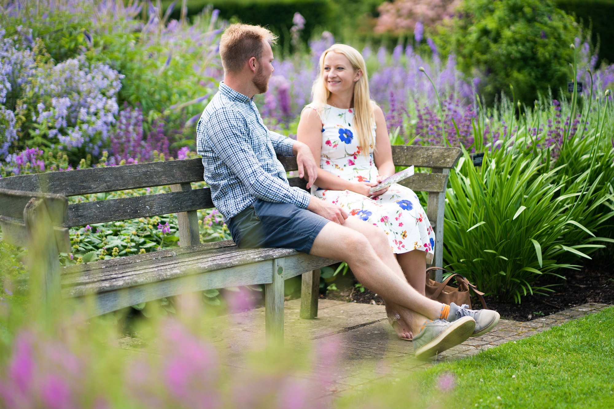 A couple sit on a bench in The Savill Garden, surrounded by purple flowers.