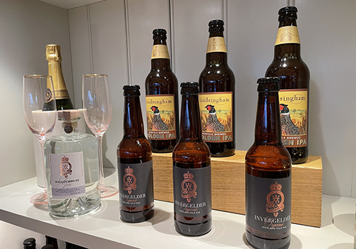 Six bottles of ale stand in a display shelf beside a bottle of sparkling wine.