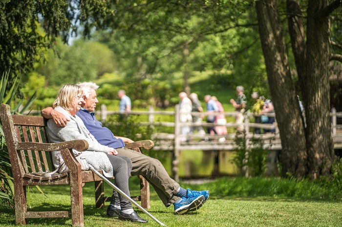 Couple sitting on a bench in The Savill Garden with a group of visitors in the background.