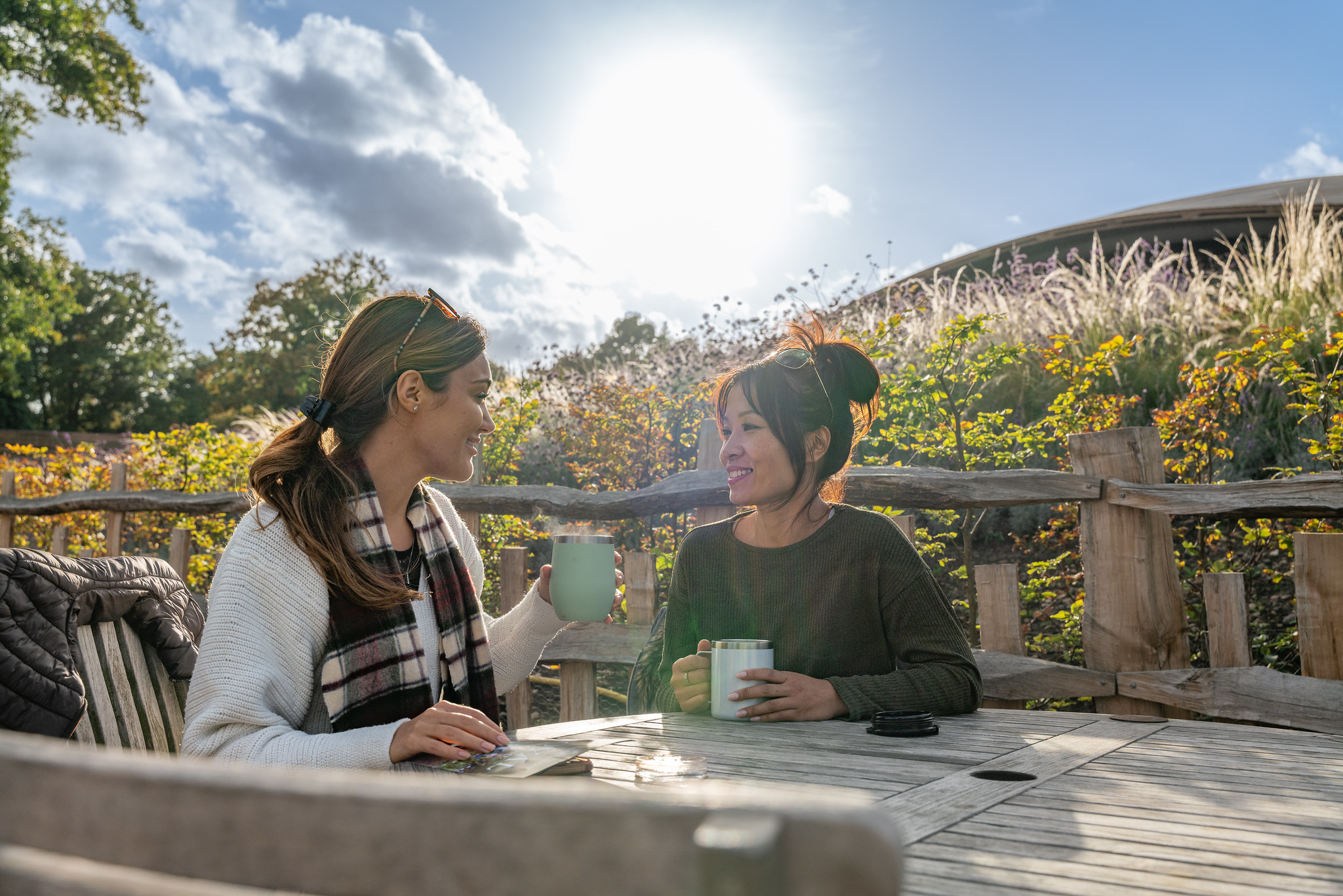 Couple sitting outside The Savill Garden Visitor Centre drinking from re-usable cups. 