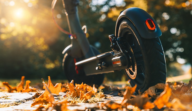E-scooter on its stand outdoors amongst fallen leaves.