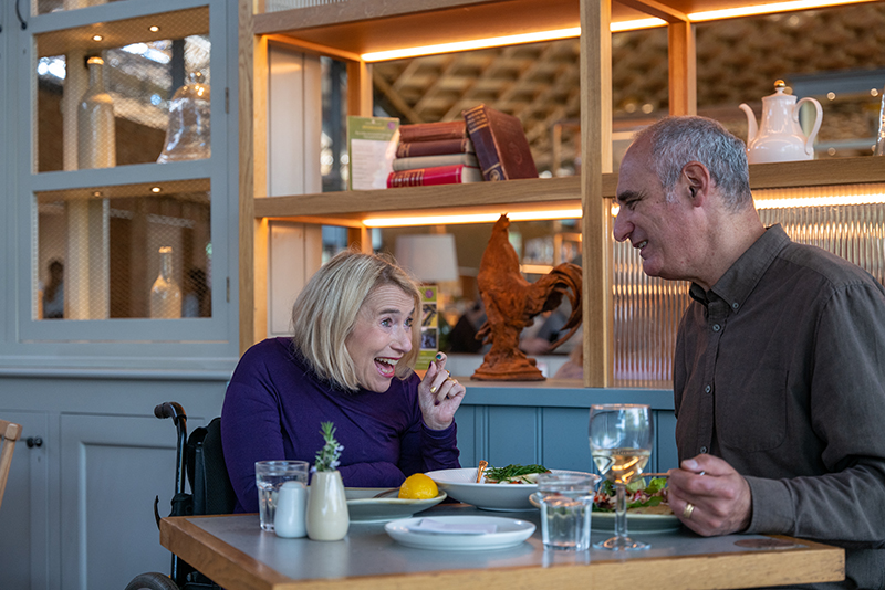 Two people sitting at a table and eating a meal. Shelves line the background.