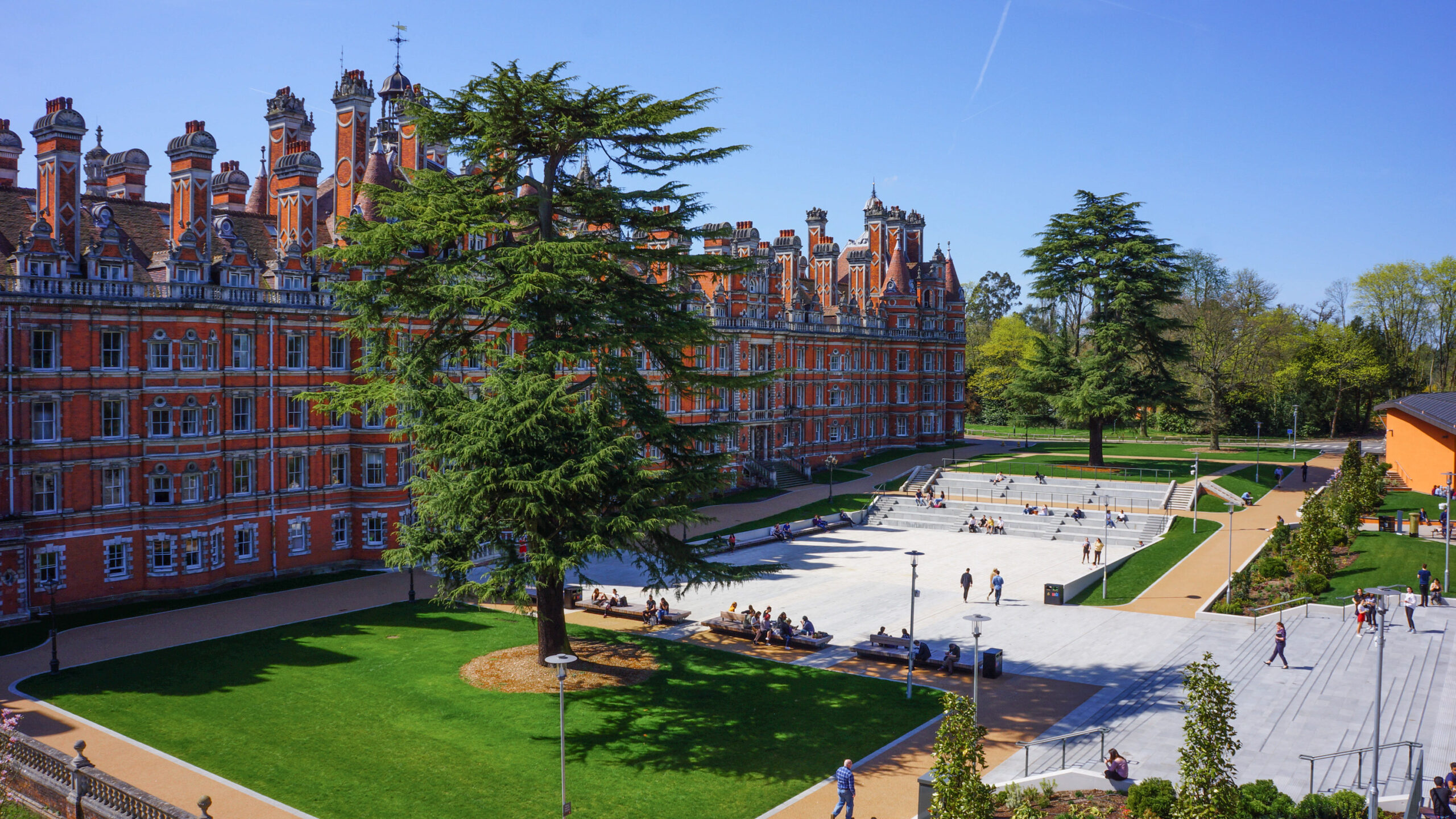 Royal Holloway main building with square and students sitting on steps.