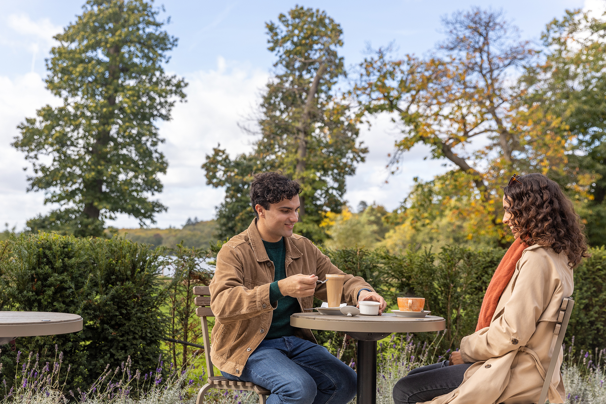 A couple sit outside the Virginia Water Pavilion with hot drinks.