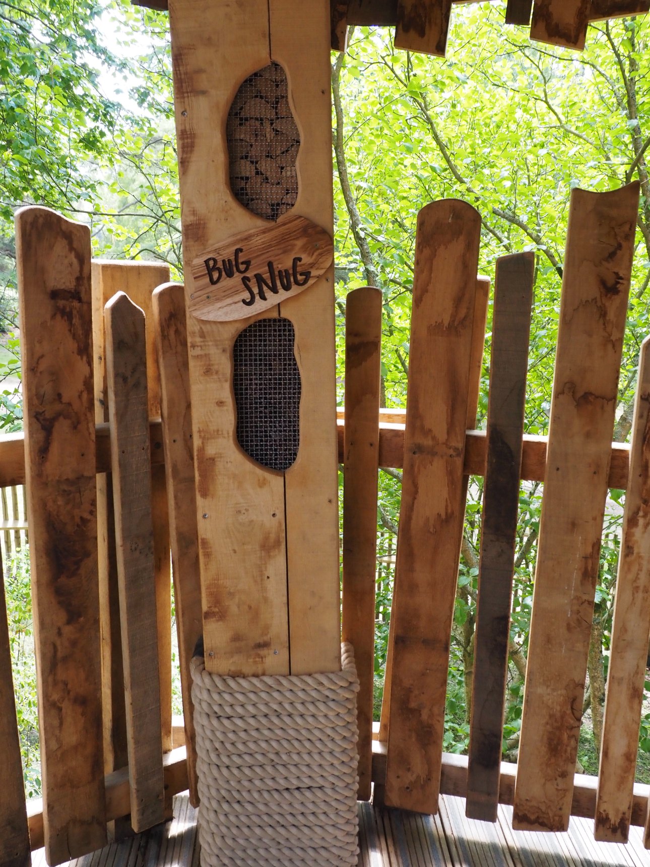 A close up of a logs and branches placed inside the cavity of a wooden beam. Underneath is a sign that reads 'Bug Snug'.