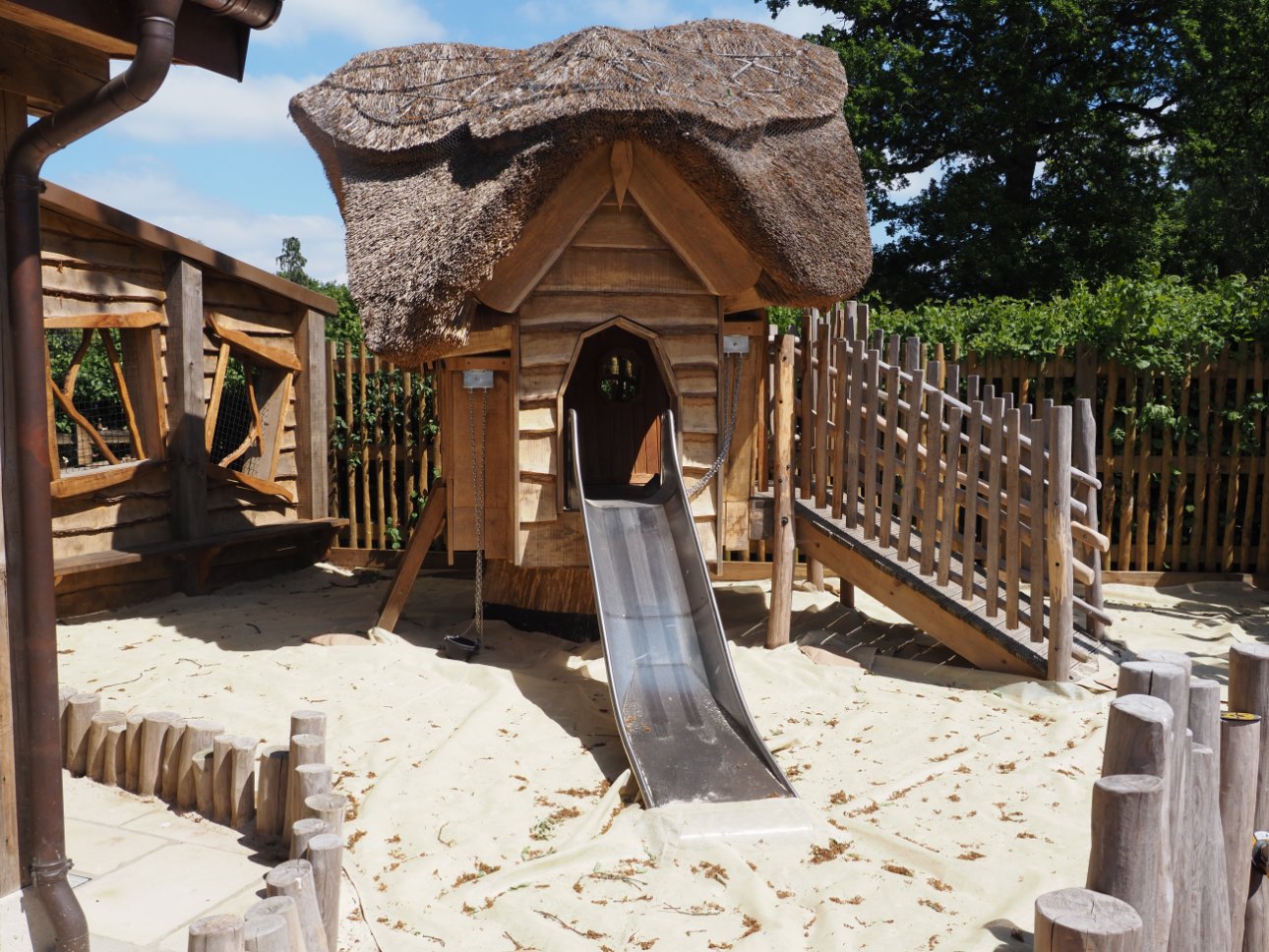 Children's slide from a thatched hut, surrounded by golden sand.