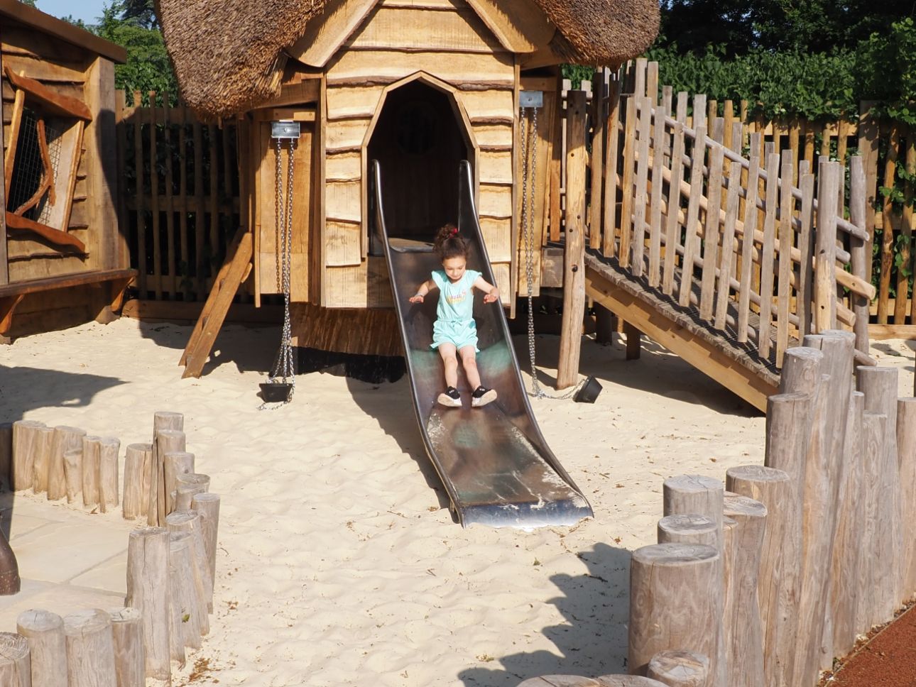 Young child sliding down a slide into golden sand.