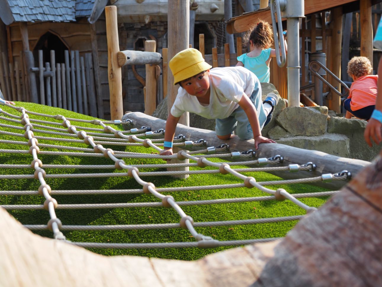 Young person wearing a yellow hat scrambling across a rope net.