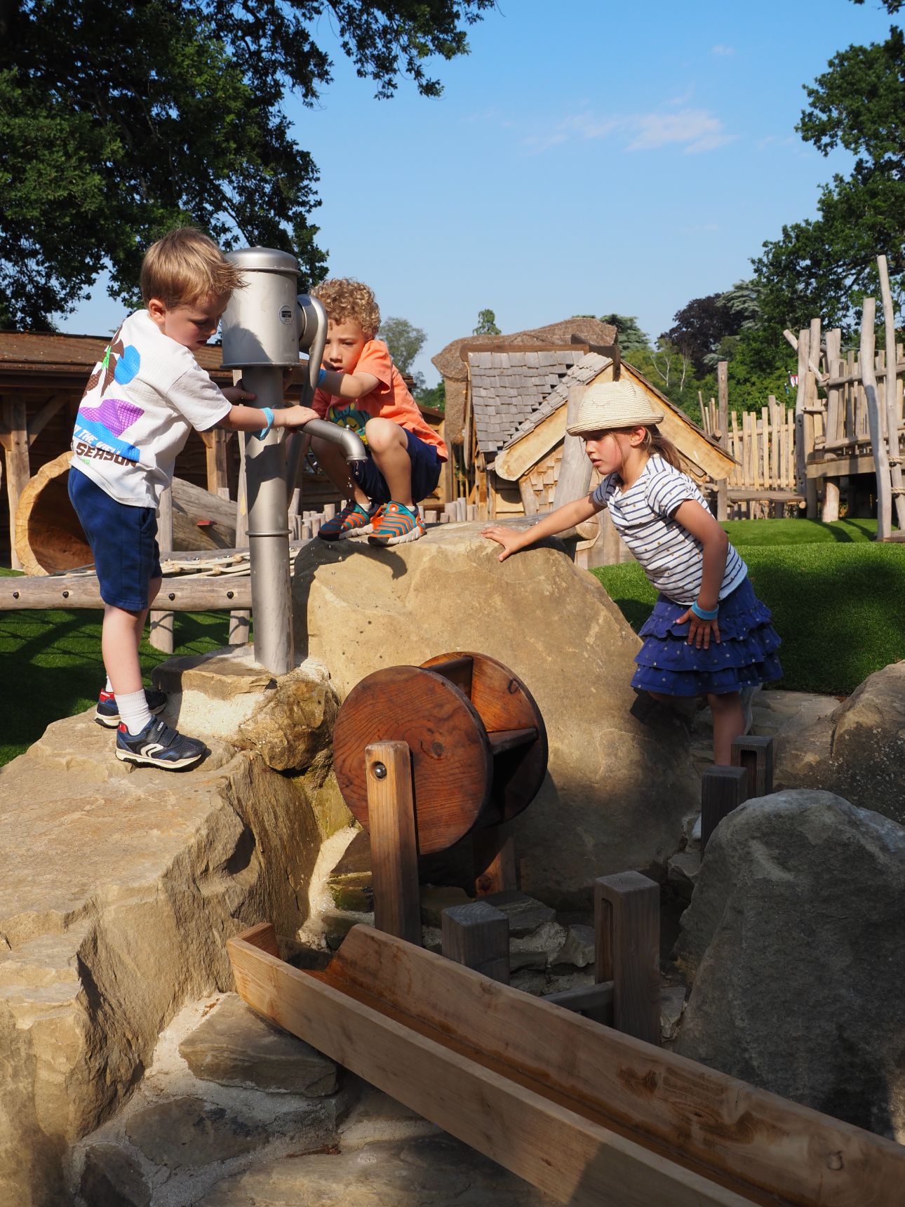 Three young children standing on rocks playing with a water pump.