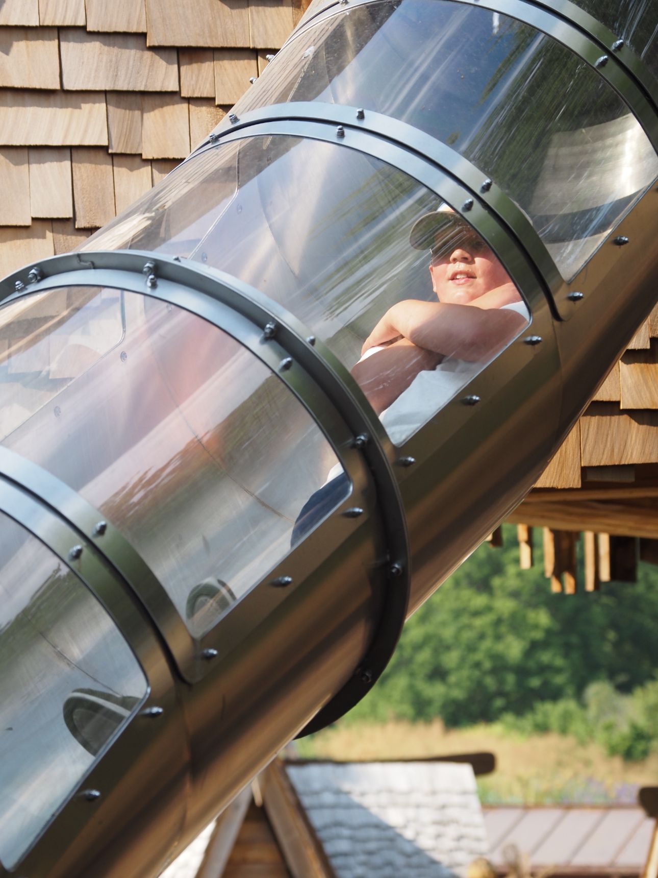 Young child sliding down a Perspex covered slide with their arms crossed.