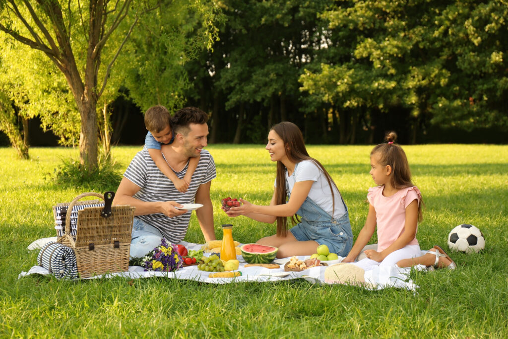 Family having a picnic on the grass sitting on a blanket with a picnic basket.