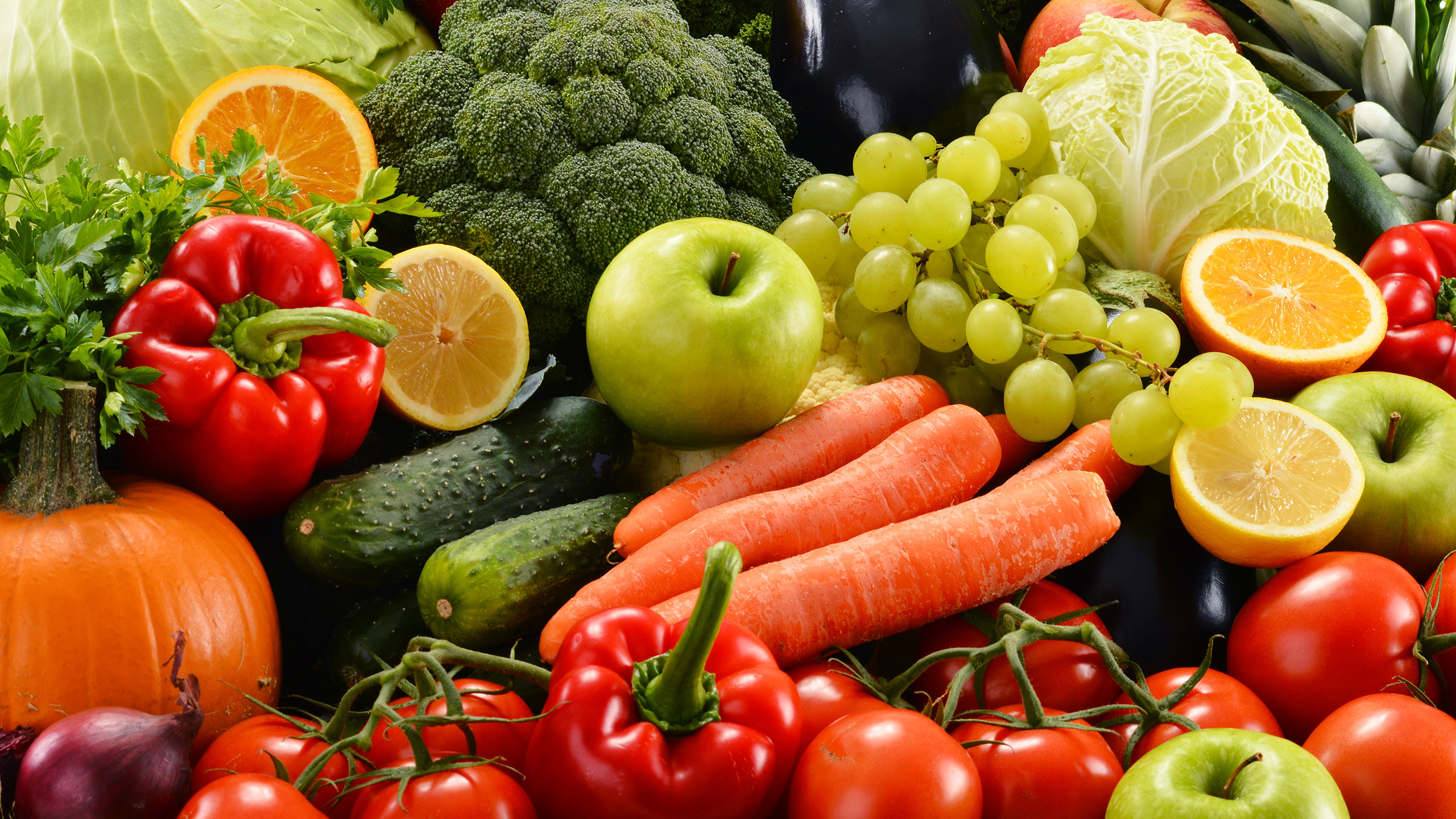 The picture is filled with produce including carrots, broccoli, red peppers, green apples and a pumpkin.