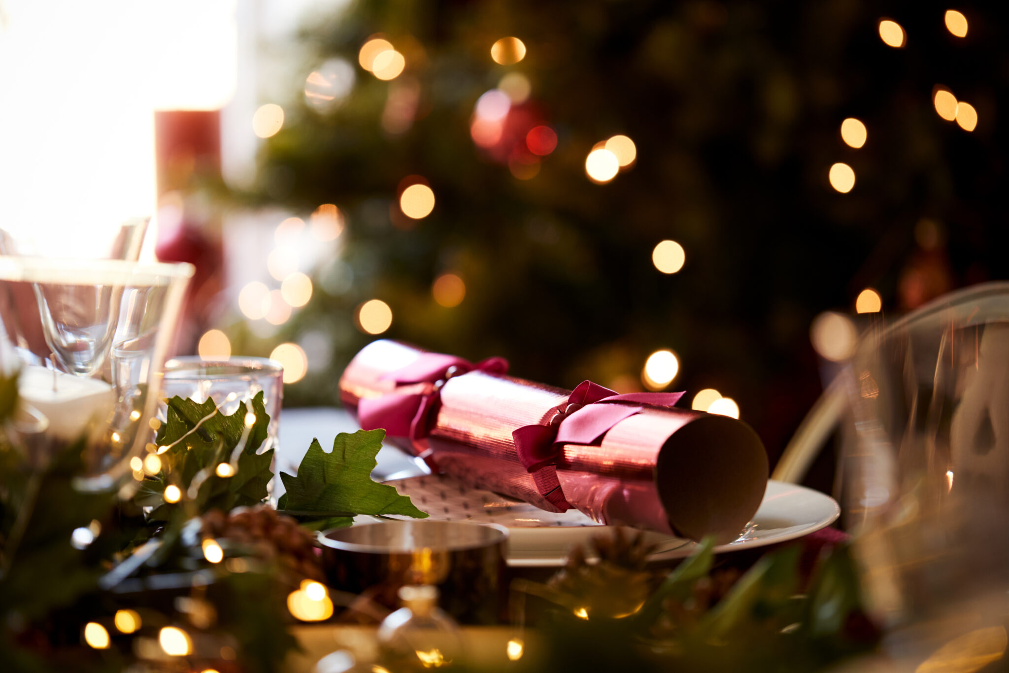 A table dressed for Christmas with a Christmas cracker laid across a plate.