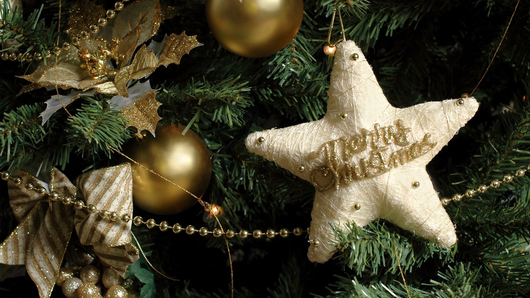 Woven white star in cream and gold with Merry Christmas embroidered on to it. Hanging on a fake green foliage tree.