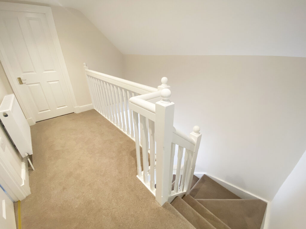 A carpeted and white walled landing with wooden banister in 6 Home Farm, Bagshot Park
