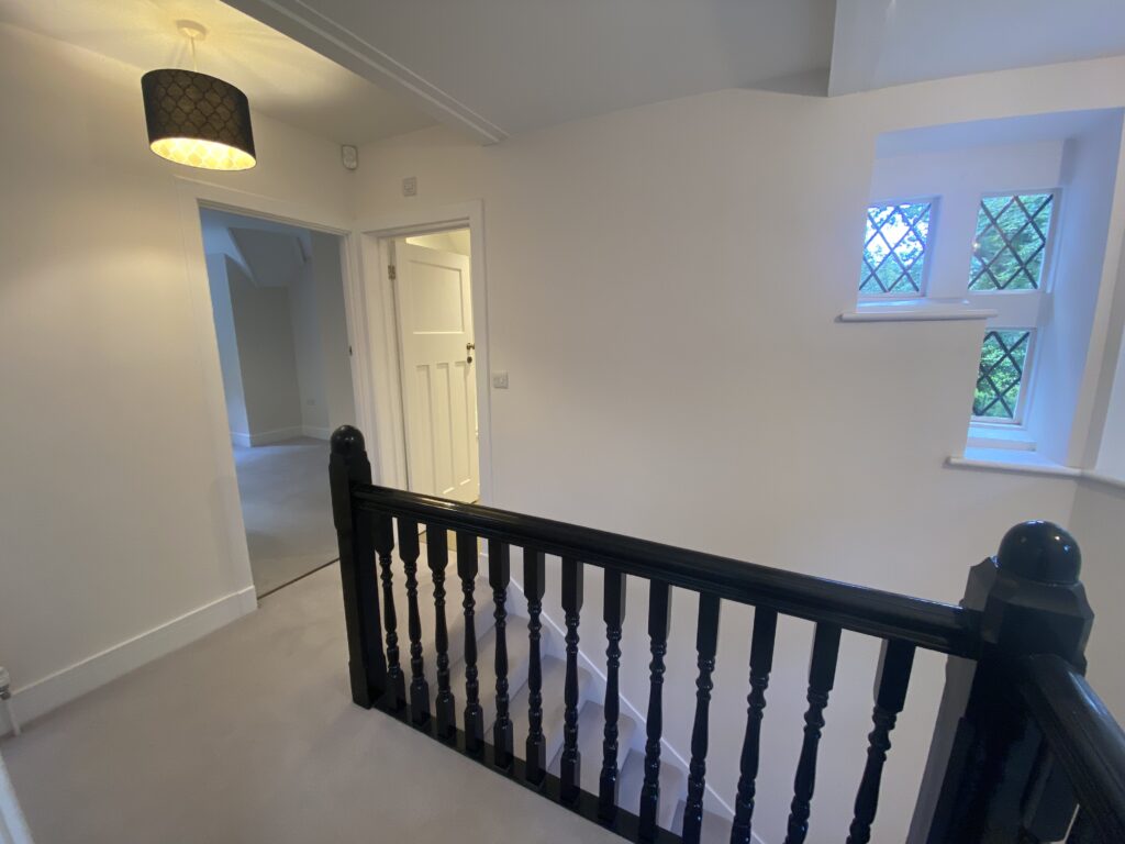 A carpeted and white walled landing with wooden banister in Pinewood Lodge, Swinley Road, Ascot, SL5 8BA
