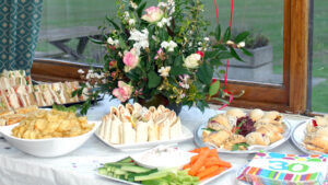 Plates of food rest on a table, with a floral arrangement behind
