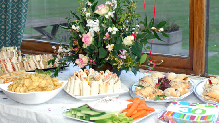Plates of food rest on a table, with a floral arrangement behind