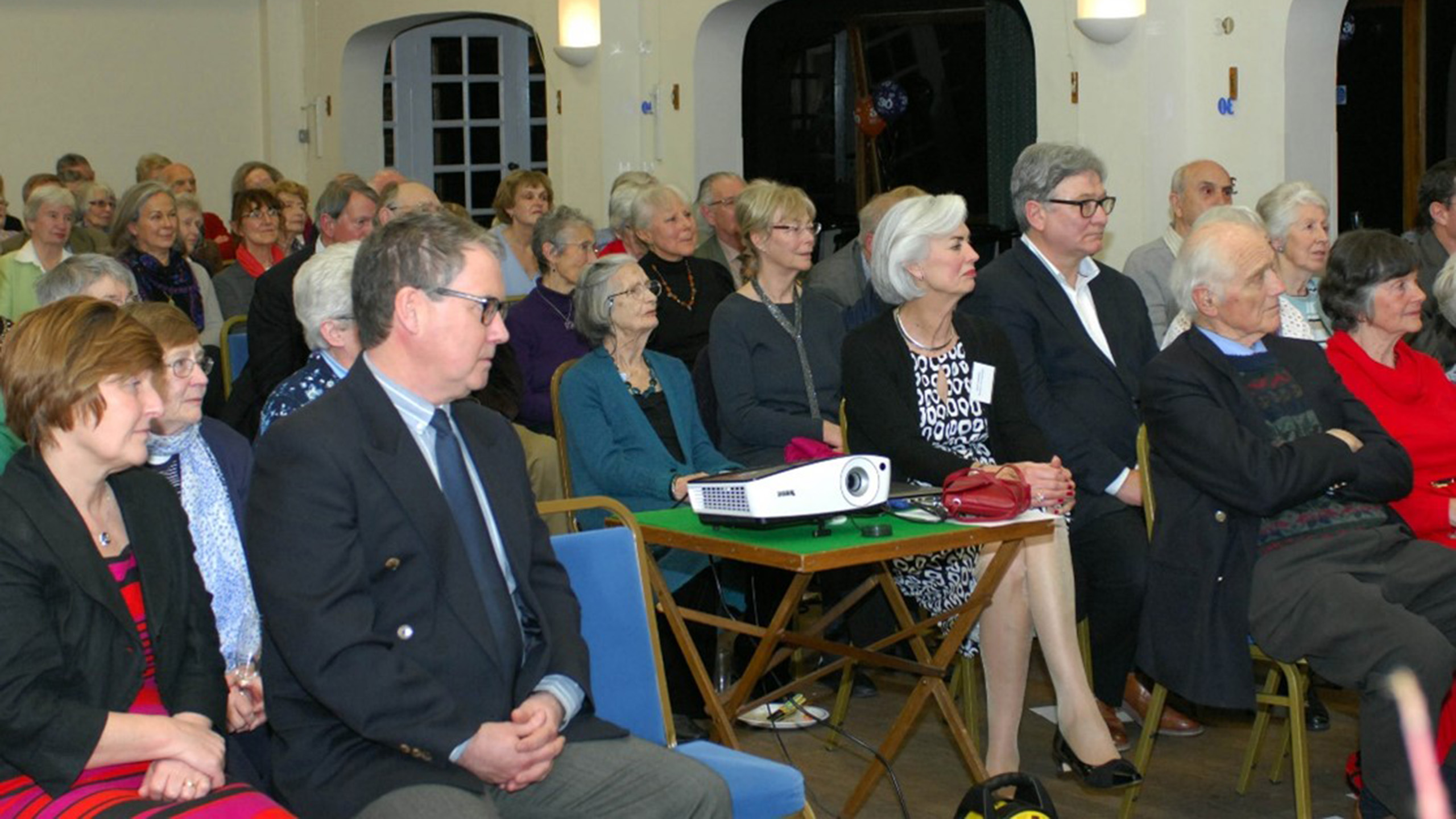 Rows of people sit on chairs looking at a presentation off screen