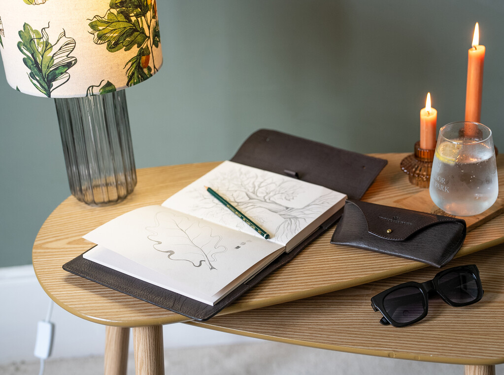 A selection of Billy Tannery Leather goods displayed on a nest of tables with two lit candles.