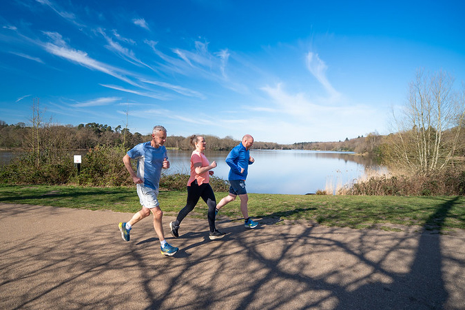 Three adult runners with Virginia Water Lake in the background.