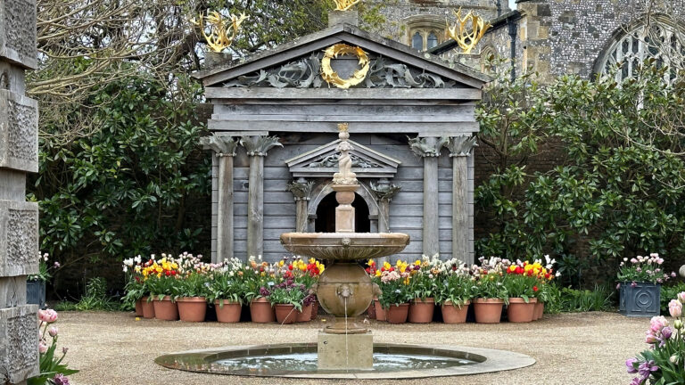 A central water fountain with containers of tulips behind.