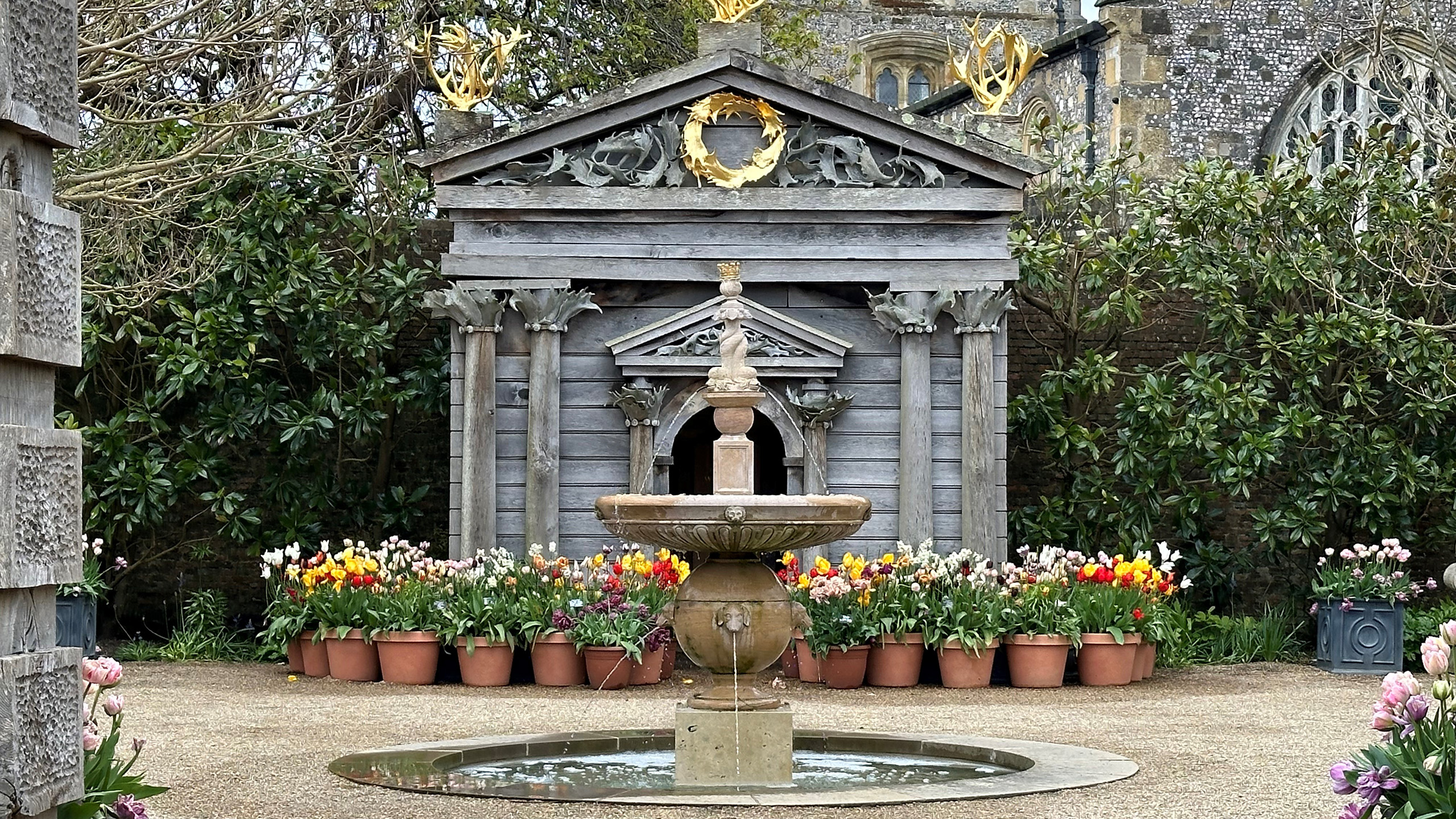 A central water fountain with containers of tulips behind.