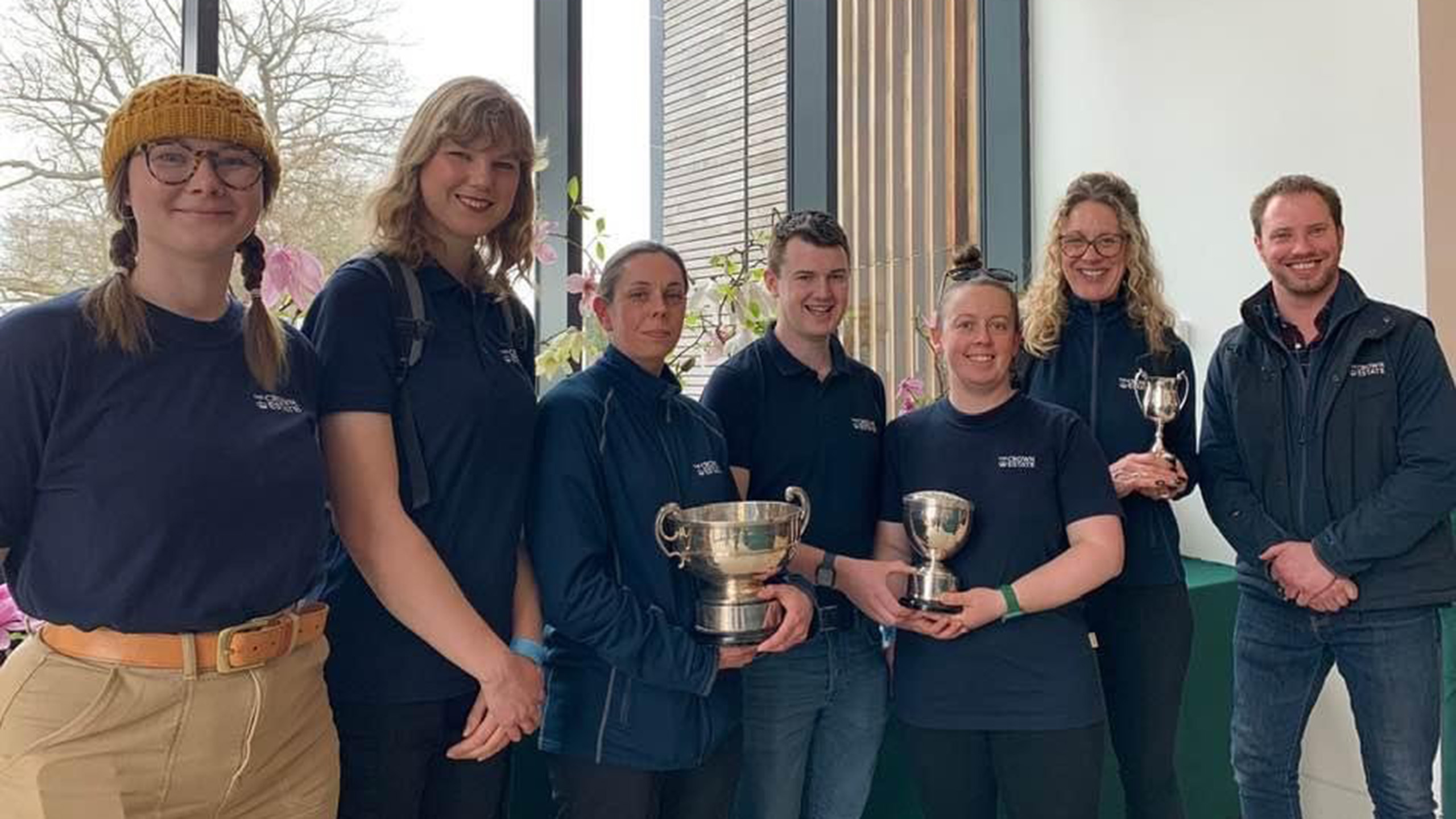 Members of the Gardens team standing in a line and holding trophies.