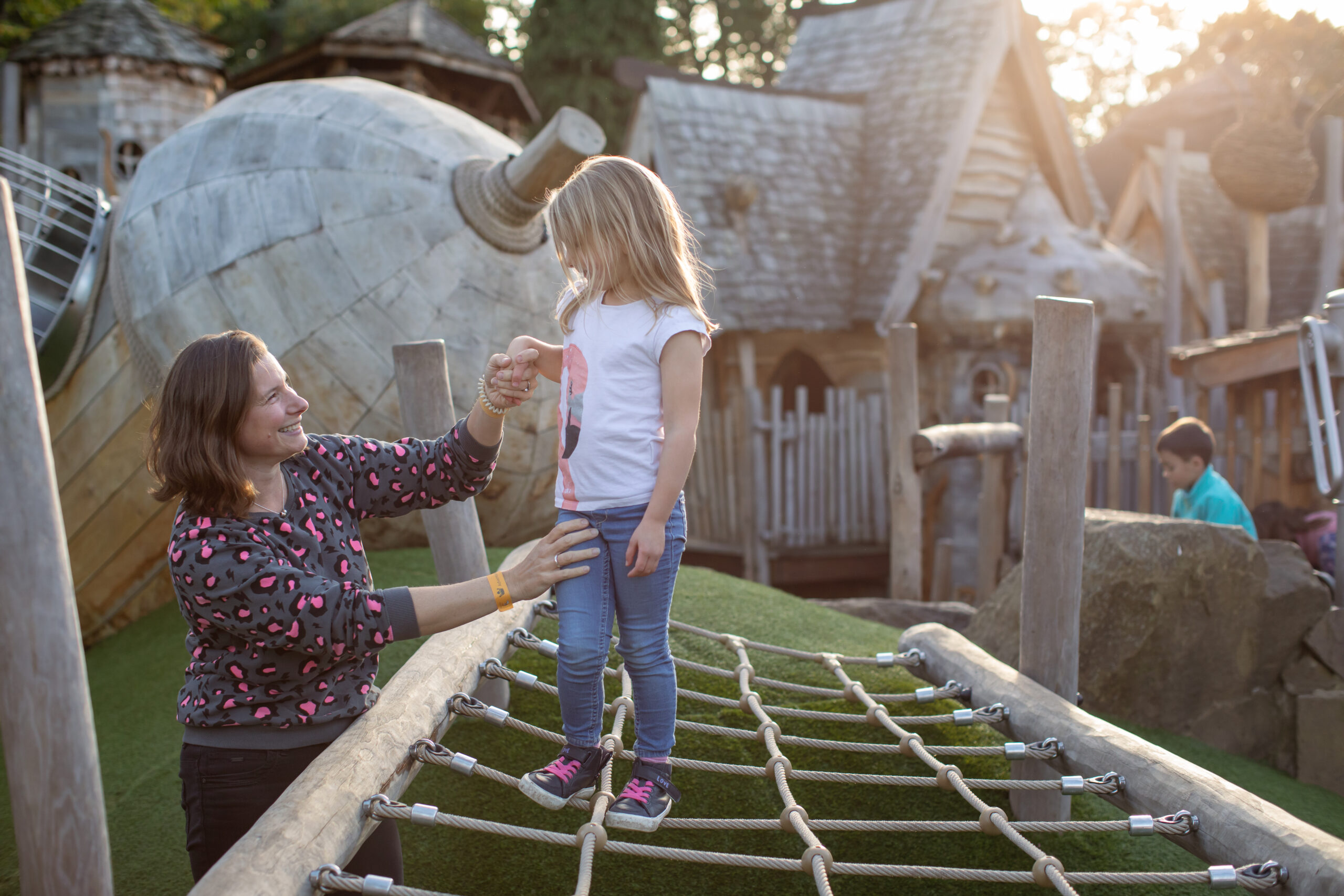 Young child walking on a rope net, supervised by an adult.
