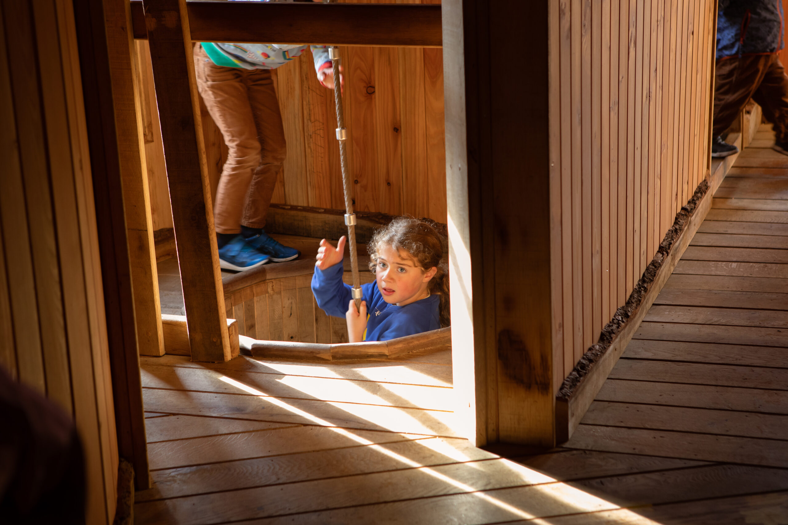 Young child climbing up a rope, supported by another child.