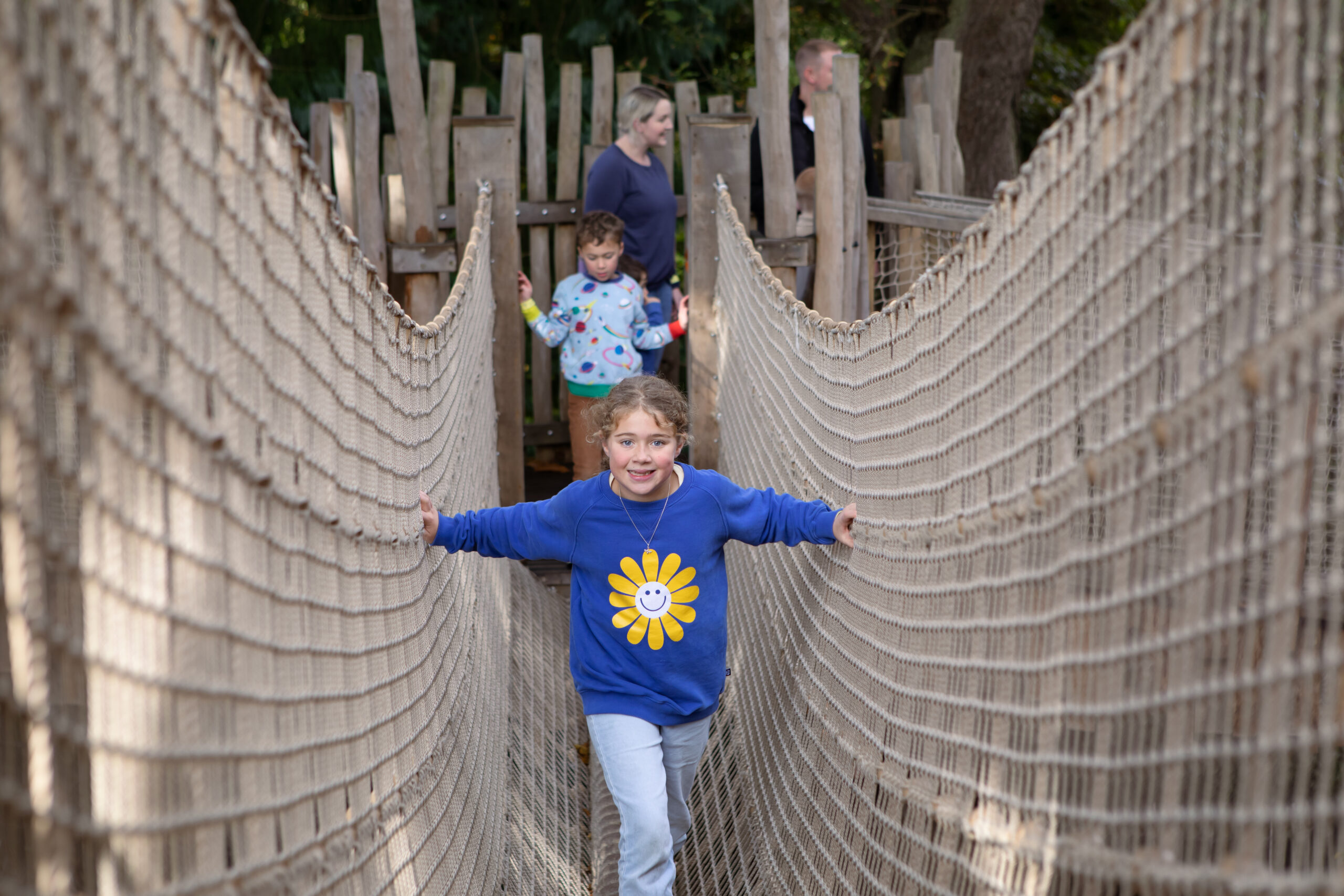 Two young children on a rope net at Adventure Play with an adult in the background.