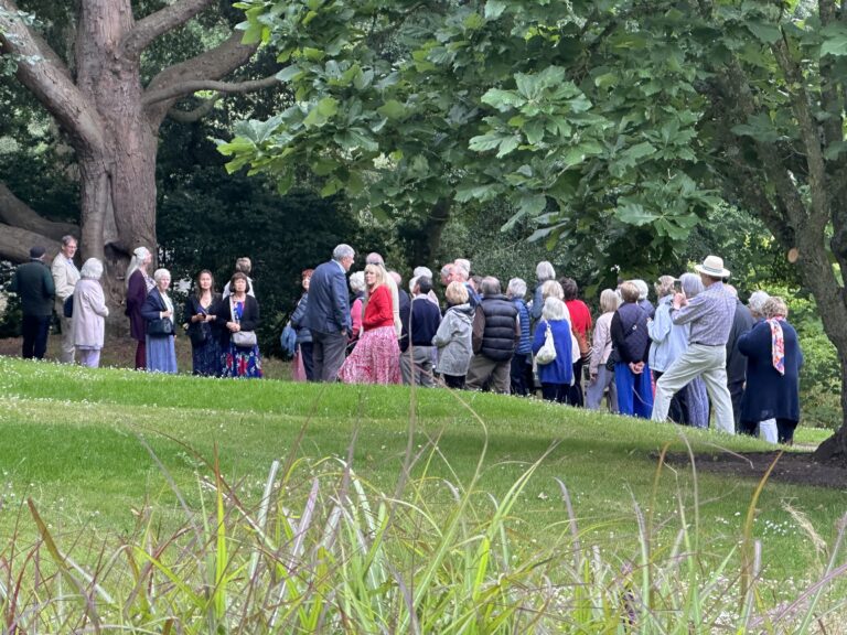 People on a guided walk in a Garden, with a green lawn in front of them.