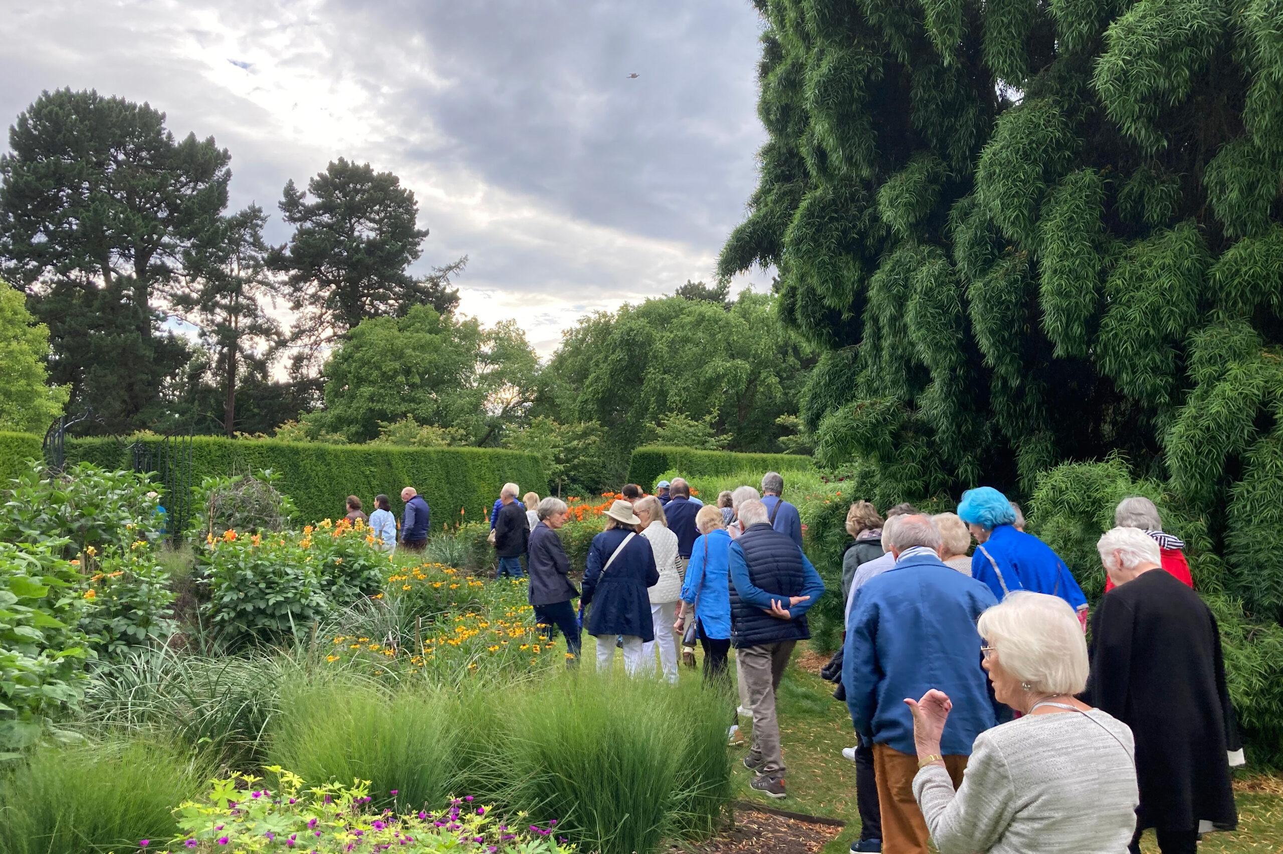A group of people on a guided tour around a Garden of seasonal borders and clipped hedges.