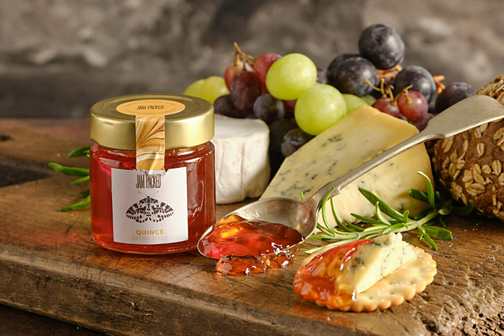Jam Packed Jam on a wooden board with a selection of cheeses and grapes.