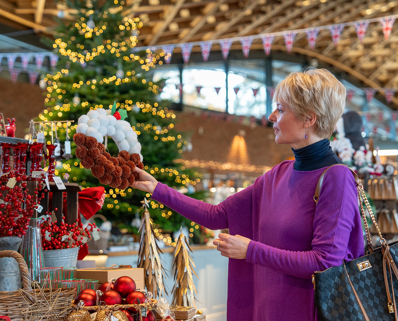 Adult wearing a cerise jumper looking at Christmas decorations. 