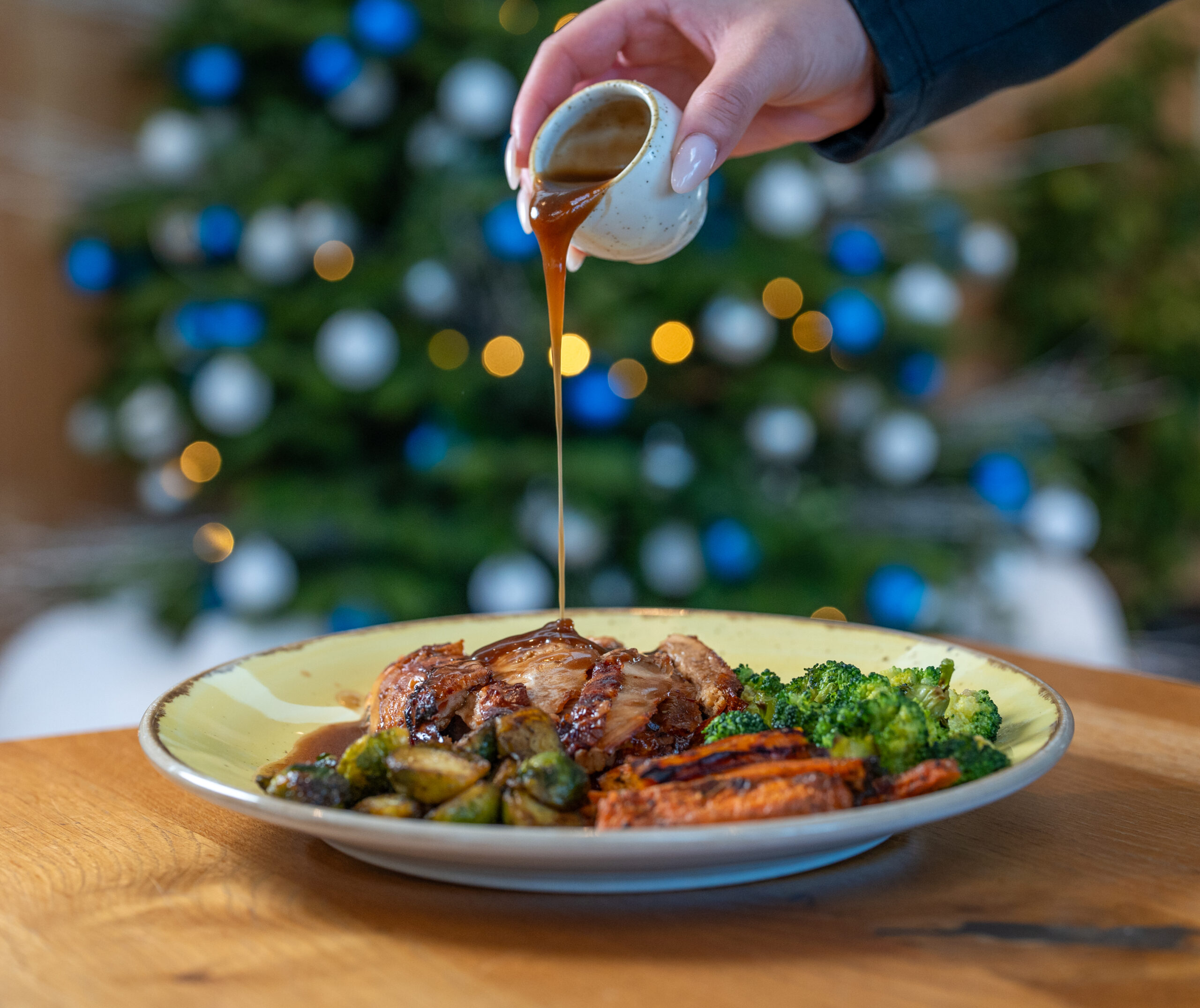 Pouring gravy on to a roast lunch with a Christmas Tree in the background.