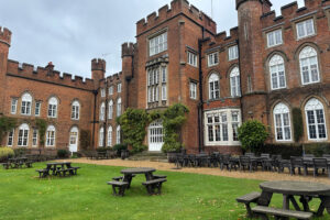 A grass lawn of picnic tables with Cumberland Lodge behind.