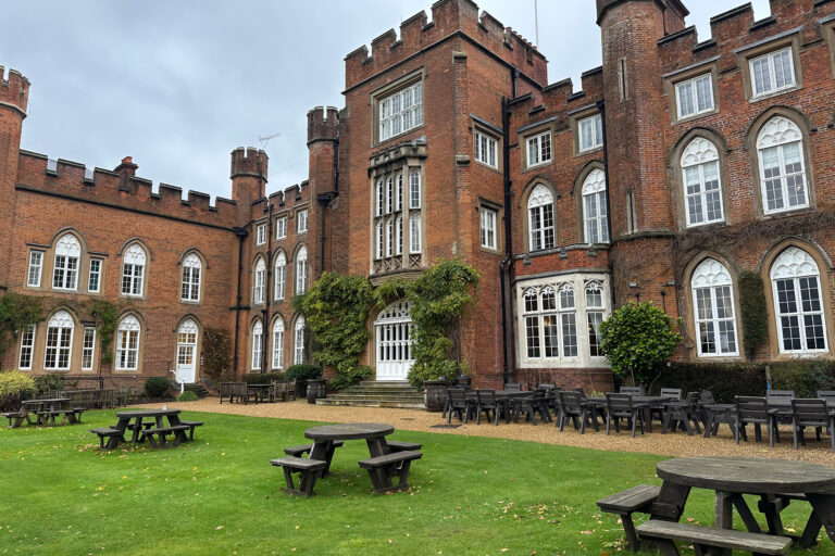 A grass lawn of picnic tables with Cumberland Lodge behind.