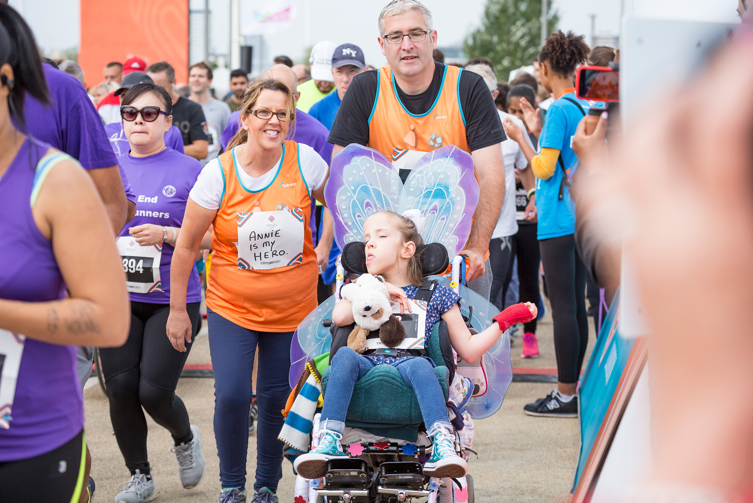 A child in a wheelchair with two adults wearing tabards for a race.