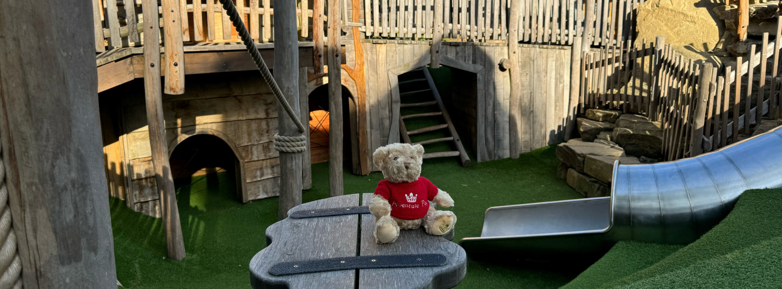 Bear with a red jumper sitting on a wooden platform.