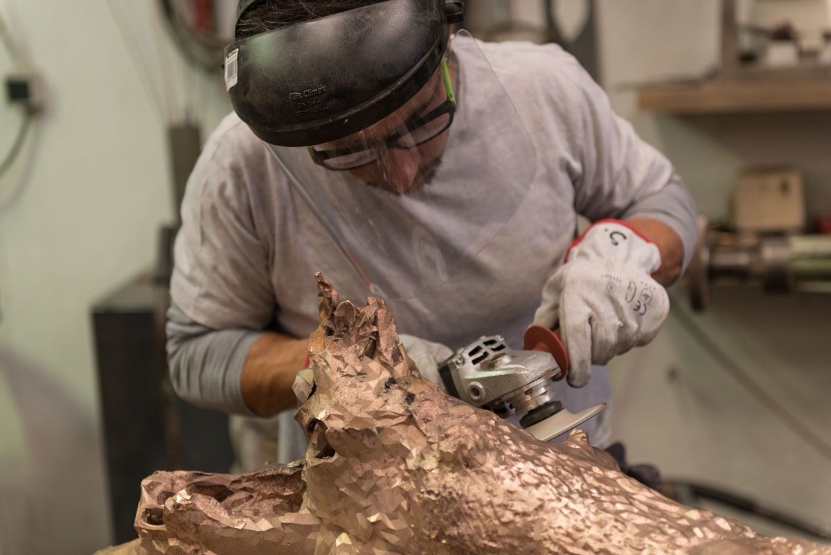 A person using machinery to make final touches to the Bronze Oak sculpture.