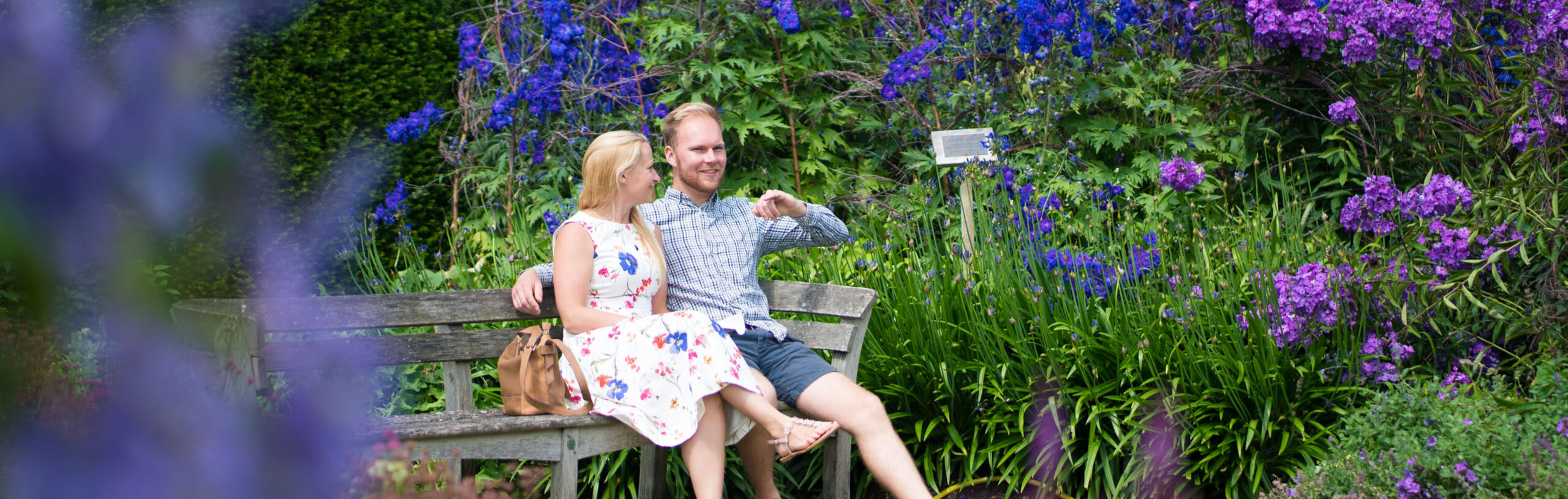 Two adults sitting on a bench in The Savill Garden surrounded by purple and pink flowers.