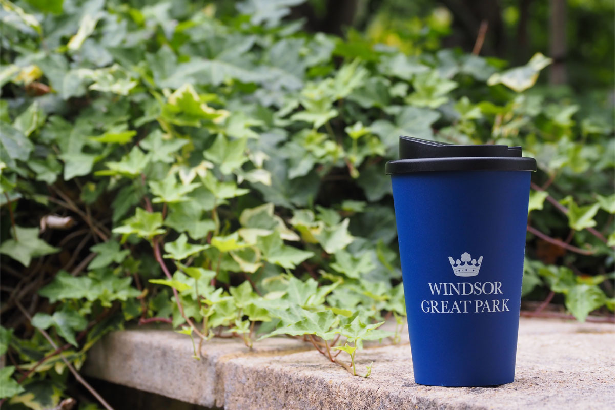 A blue reusable cup beside green shrubs.