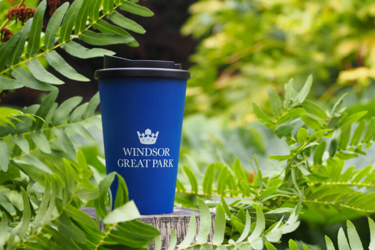 A reusable cup on a post beside green shrubs.
