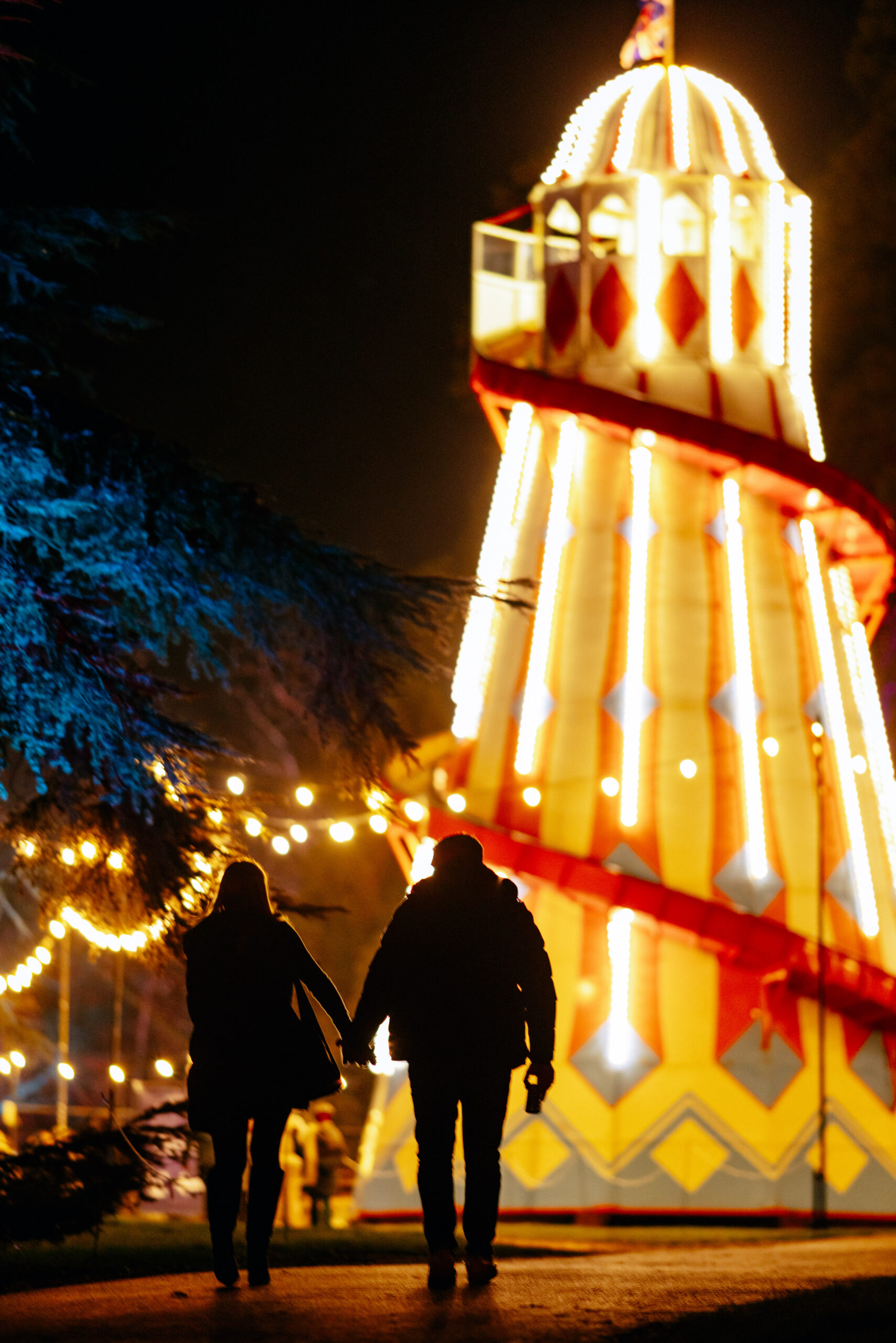 Two people walking towards a brightly lit Helter Skelter.